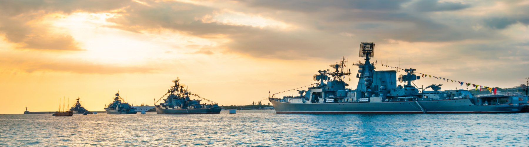 Naval ship cutting through ocean waves, with radar equipment visible against a blue sky.